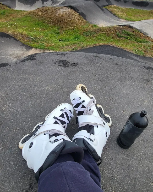 Białe rolki i bidon na szczycie górki pumptracku, widok oczami jadącego